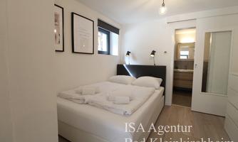 A cozy bedroom with a large bed, equipped with fresh towels. The walls are bright and there are windows that let in daylight.