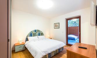 A modern bedroom with a large bed and wooden floor. There is a window that overlooks a small outdoor area.