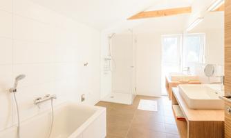 A modern bathroom with a bathtub and a shower. Large windows provide plenty of daylight.