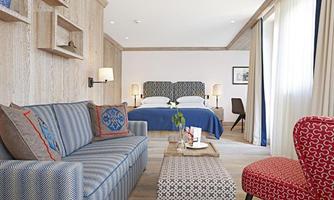 A bright and modern hotel room with a cozy sofa, a table, and a large bed in the background. The decor is stylish and inviting.
