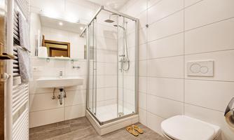 A modern bathroom with a shower cabin and bright tiles. There is a sink and a toilet, as well as a towel radiator.
