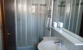 A small bathroom with a shower cabin and a sink. The walls are brightly tiled and there are towels and toiletries nearby.
