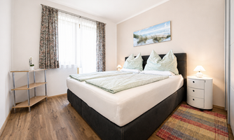 A cozy bedroom with a large box spring bed and colorful pillows. The room has a bright atmosphere and a beautiful view and balcony.