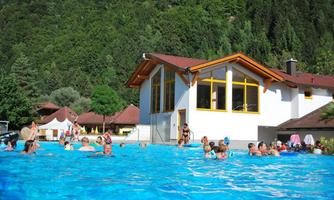 A pool full of people, surrounded by green trees and huts. The clear water reflects the sun, creating an inviting atmosphere.