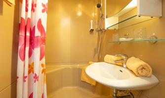 A small, bright bathroom with a bathtub and a sink. The shower curtain is decorated with colorful floral patterns.
