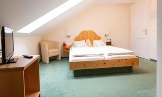 A cozy bedroom with a double bed and a television. There is a comfortable armchair and a wooden table.