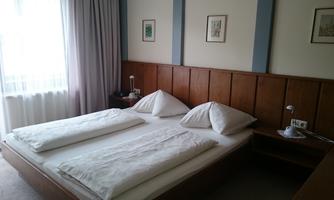 A simple bedroom with two single beds and white bedspreads. There is a wooden wardrobe and some pictures on the wall.