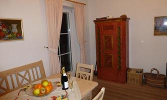A cozy dining area with a wooden table and chairs. In the background, there is a colorful cabinet and a table decorated with fruit.