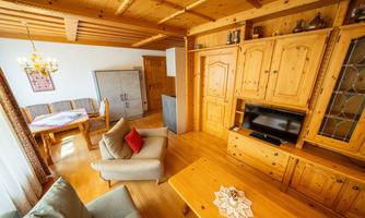 A cozy living room with wooden decor and light wooden flooring. There is a seating area, a table, and a TV cabinet.