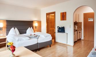 A cozy bedroom with a double bed and a small dining table. The decor is bright and modern, with access to a kitchenette.