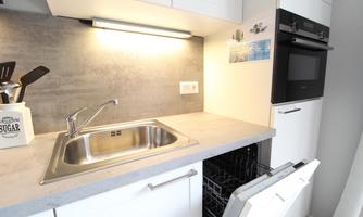 A modern kitchen with a stainless steel sink and a dishwasher. The walls are light and the lighting is warm and inviting.
