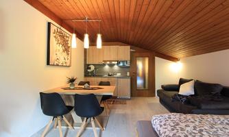 A cozy apartment with wooden ceilings and modern furnishings. The dining area is bright and inviting, with a table and elegant chairs.