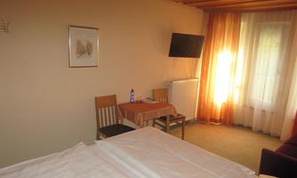 A simple hotel room with a double bed, a table, and two chairs. Additionally, there is a television and large windows with orange curtains.