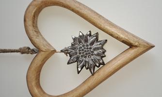 A wooden heart hangs on a string. In the middle is a silver, blooming ornament.