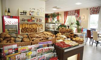An inviting bakery with a large selection of fresh bread and pastries. In the background, drinks and magazines are visible.