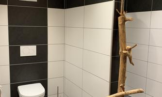 A modern bathroom with black and white tiles. It includes a toilet and a stylish wooden stand.