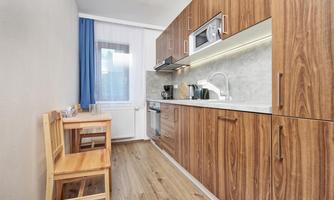 A modern kitchenette made of wood with a microwave and a stove. A small table with a chair complements the space.