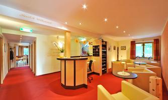 A bright reception area with red carpets and comfortable seating areas. The walls are designed in a friendly manner, and there is a reception counter.
