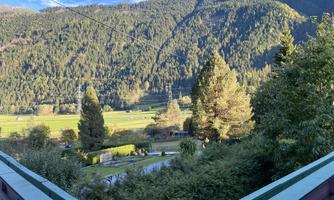 A beautiful view of green meadows and high mountains. The landscape is surrounded by trees and features clear blue skies.