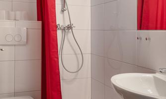A small bathroom with a shower and red curtains. There is also a sink and a toilet.