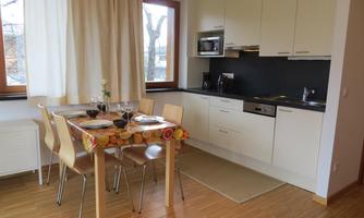 A modern kitchen with a dining table and chairs. Bright colors and large windows provide plenty of daylight.