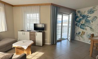 A cozy living area with a sofa, a television, and beautiful wall decoration. Large windows provide plenty of daylight and a view outside.