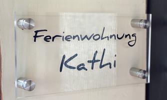 A transparent sign with the inscription "Vacation Apartment Kathi". It is mounted on a wall.