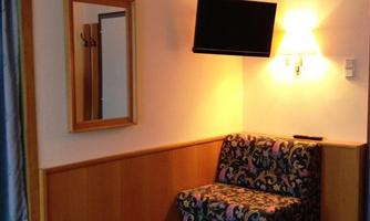 A cozy room with two beds, a television, and a comfortable armchair. The room is bright and cheerfully designed.
