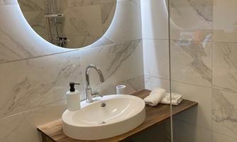 A modern bathroom with a round mirror and a sink on a wooden shelf. The walls are clad with light tiles.