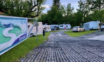 A quiet campsite with motorhomes and trees. The path is coated with gravel and there is a large sign that reads "Lake-Alm Steindorf".