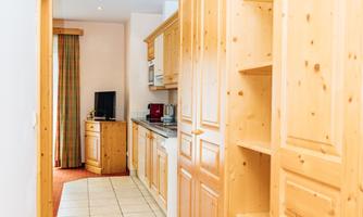 A bright hallway with wooden cabinets and a tiled floor. At the end of the hallway is a kitchen, and a carpet adds a cozy atmosphere to the room.
