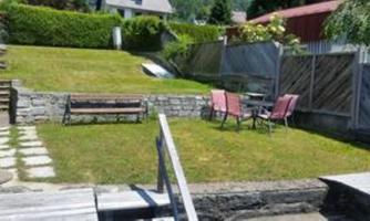 A beautiful garden with a green lawn and a bench. In the background, two chairs are placed at a table.