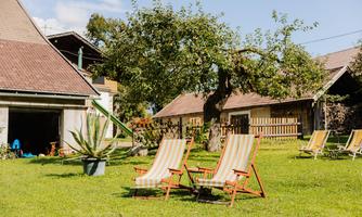 Two loungers are standing on a green meadow in front of a farmhouse. In the background, trees and more loungers can be seen.