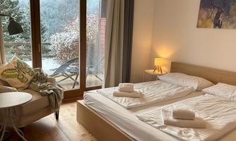 A cozy bedroom with two single beds and a small table. Large windows provide a view of the snowy landscape outside.