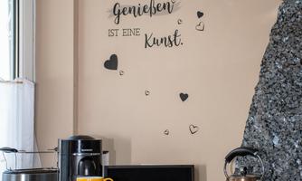 A modern kitchen with a granite surface and various kitchen utensils. Inspirational quotes about food and enjoyment are decoratively displayed on the wall.