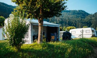 A campsite with a caravan and a cozy awning. Surrounded by green meadows and hilly landscape.