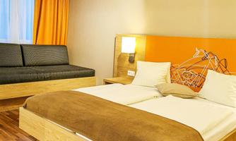 A modern hotel room with a double bed and a cozy sofa. The walls are in light colors and the atmosphere is inviting.