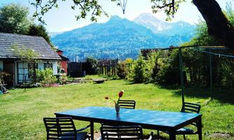 A beautiful garden with a table and chairs under a tree. Mountains are visible in the background.