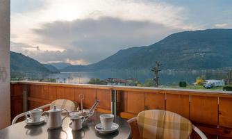 A beautiful view of a lake with mountains in the background. On the table are cups and a coffee pot, ideal for a relaxing break.