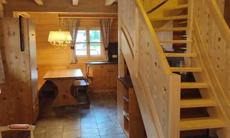 A cozy room with wooden details and a staircase. In the background, a table and chairs are visible.