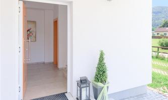 An inviting entrance area with modern, open doors. In front of the door stands a well-maintained plant and a lantern.