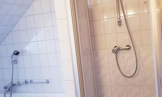 A bathroom with a shower cabin and a bathtub. The walls are tiled and the ceiling is made of wood.