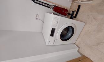 A washing machine is located in a corner of the room. Next to it are a vacuum cleaner and a clothes drying rack.