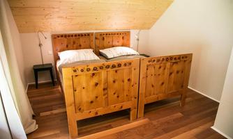 A cozy bedroom with a rustic wooden bed and clean lines. The floor is made of wood, and the walls are bright and inviting.