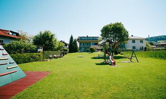 A playground with a slide and a swing on a green meadow. In the background, several houses and trees can be seen.
