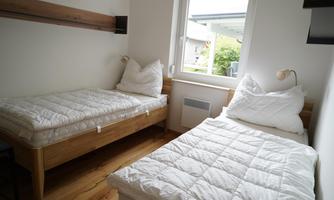 A simple bedroom with two single beds and a large window front. The rooms are bright and friendly designed.