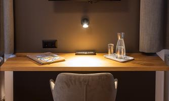 A cozy workspace with a modern desk and a comfortable chair. On the wall hangs a television with the logo "Ertlhof Familiengut".