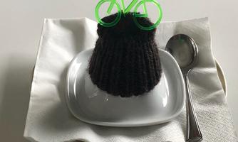 A chocolate cake with a green bicycle decoration on a small plate. Next to it, a spoon lies on a piece of napkin.