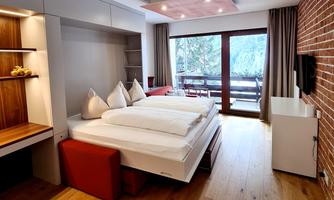 A modern bedroom with a cozy bed and wooden floor. Large windows allow plenty of daylight and offer a view outside.
