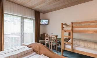 A cozy room with two beds and a loft bed. There is a small table and a television on the wall.